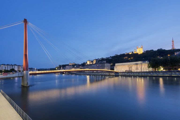 Vue nocturne de la Saône à Lyon avec la passerelle Saint-Georges illuminée et la basilique de Fourvière en arrière-plan.